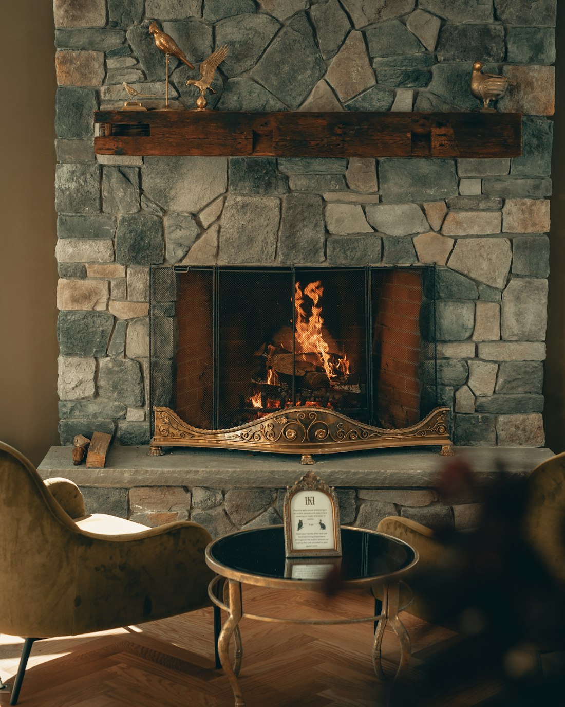 A cabin sitting room with a stone fireplace and glass onto the trees